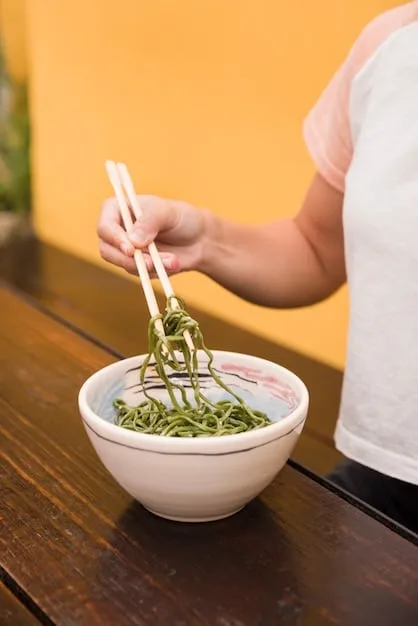A person expertly dipping zaru soba noodles into tsuyu sauce with chopsticks, ready to enjoy. The focus is on the interaction of noodles and sauce, with a shallow depth of field highlighting the textures.