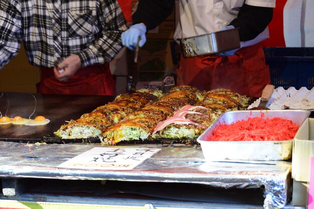 A bustling street food market in Osaka, with vendors selling a variety of dishes such as takoyaki, okonomiyaki, and yakitori. The scene is lively and colorful, with people enjoying the food and the vibrant atmosphere.