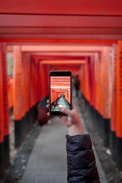 A close-up shot of a smartphone screen displaying a Japanese train map app, showing various train lines, station names in both English and Japanese, and arrival/departure times. A hand is holding the phone, with a blurred background of a busy train station platform.
