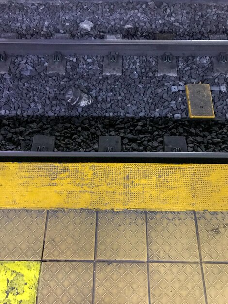 A clear, well-lit train platform in Japan. There are yellow tactile paving stones for the visually impaired. A train is pulling into the station, and passengers are lined up neatly to board.