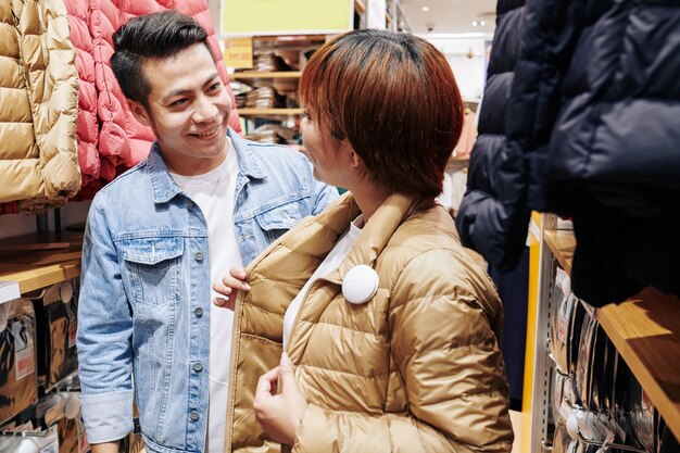 A friendly Japanese store clerk assisting a customer in a secondhand shop. The clerk is smiling and pointing to an item, while the customer looks interested and engaged.