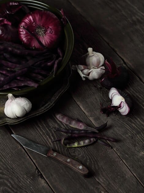A striking close-up showing several black garlic cloves arranged on a dark slate surface, with a knife beside them, showcasing their soft, almost gummy texture.