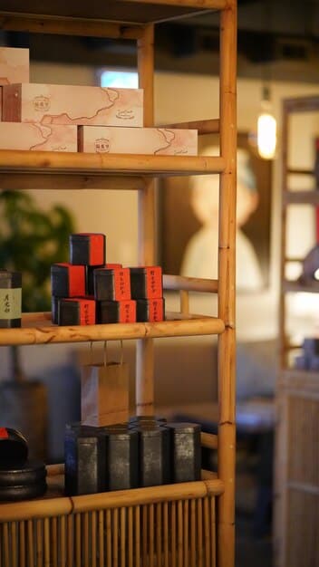 A well-stocked shelf in a Japanese tea supply store in the US, featuring neatly arranged matcha tea powders, chashaku (tea scoops), chasen (bamboo whisks), and various ceramic tea bowls. The store interior is clean, well-lit, and designed with a minimalist aesthetic.