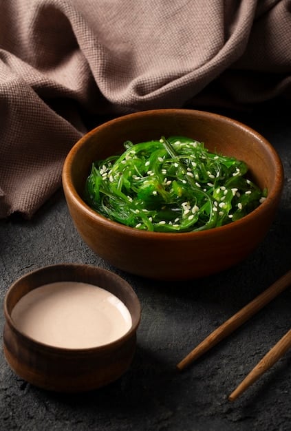 Close-up shot of vibrant green wakame seaweed salad in a small ceramic bowl, garnished with sesame seeds and a sprig of cilantro, with a blurred background of a traditional Japanese dining setting.