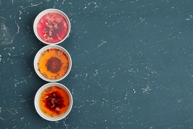 An overhead shot displaying three bowls of different dashi variations: kombu dashi (clear and light), awase dashi (slightly darker with visible sediment), and shiitake dashi (deep brown and rich). Each bowl is labeled subtly to indicate its type.