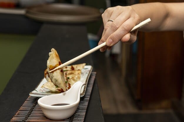 A shot of someone using chopsticks to pick up a piece of perfectly fried tempura, with steam rising from it, against a backdrop of traditional Japanese tableware.