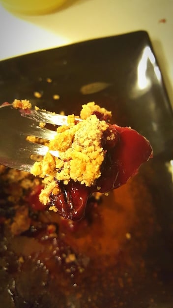 A close-up shot of a Japanese curry roux block being broken apart and added to a simmering pot of curry. The pot contains carrots, potatoes, and chunks of beef. Steam rises from the pot, suggesting a rich aroma.