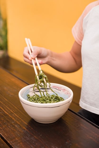 A person expertly dipping zaru soba noodles into tsuyu sauce with chopsticks, ready to enjoy. The focus is on the interaction of noodles and sauce, with a shallow depth of field highlighting the textures.