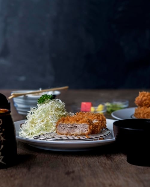A beautifully arranged plate of tonkatsu set meal, featuring the crispy pork cutlet, a bowl of fluffy white rice, shredded cabbage, miso soup, and tsukemono (Japanese pickles). The tonkatsu is drizzled with tonkatsu sauce.