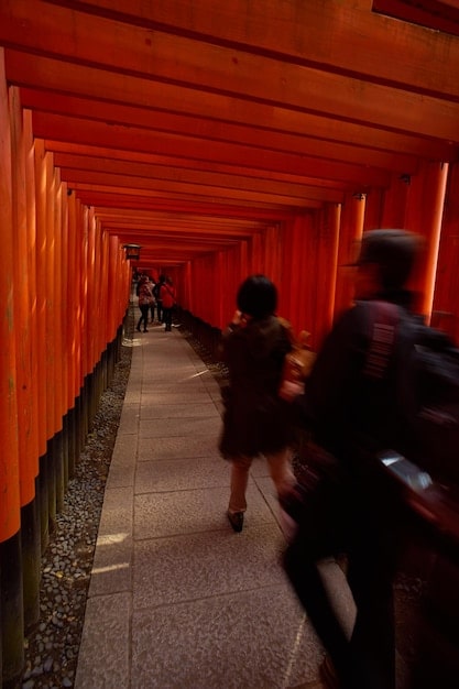 A close-up of a red torii gate at Fushimi Inari Shrine in Kyoto with sunlight streaming through. People are walking up the pathway.