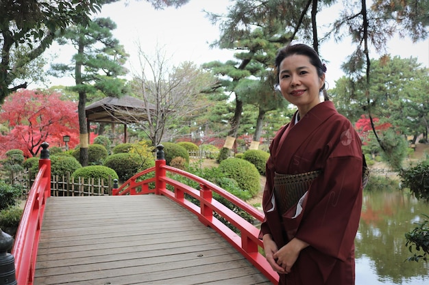 A close-up photo showing a Japanese person bowing slightly to a US traveler, with both individuals maintaining a respectful and polite expression. The scene is set in a traditional Japanese garden.