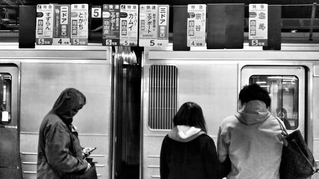 A crowded Tokyo subway station during rush hour, illustrating the efficiency and precision of public transportation, where even slight delays are prominently announced.